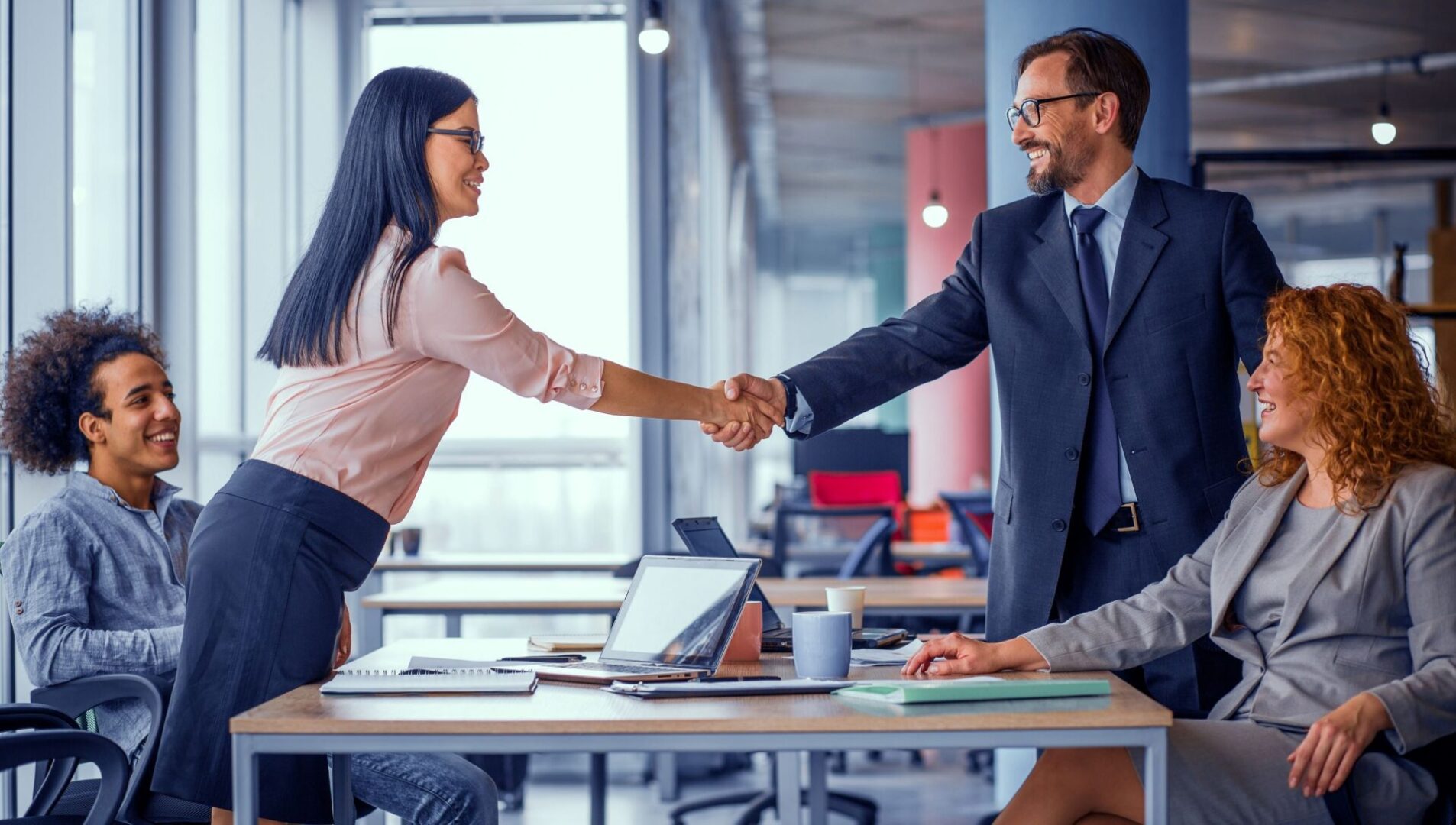 Two people shaking hands over a table in an office.